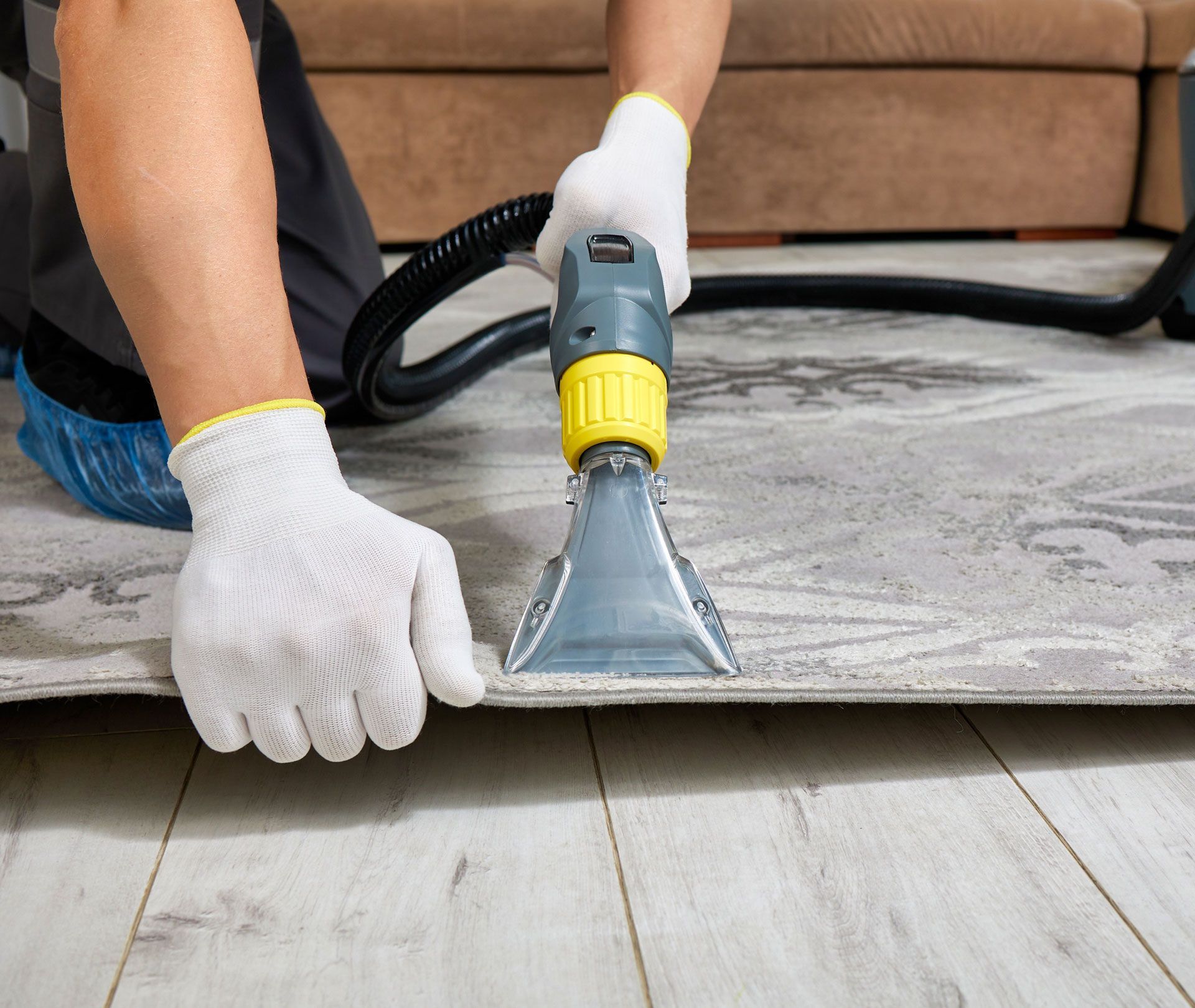 Person cleaning a gray rug with a carpet extractor on a wooden floor