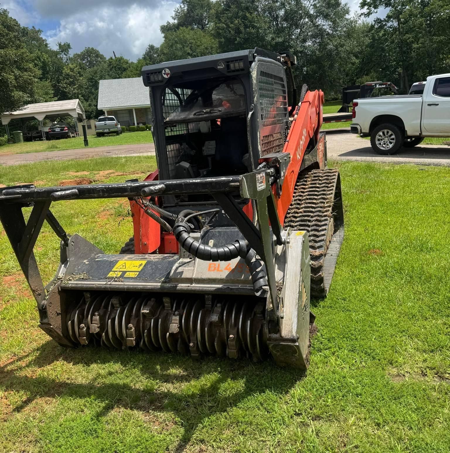Orange and black track skid steer with brush cutter attachment on a grassy lawn.