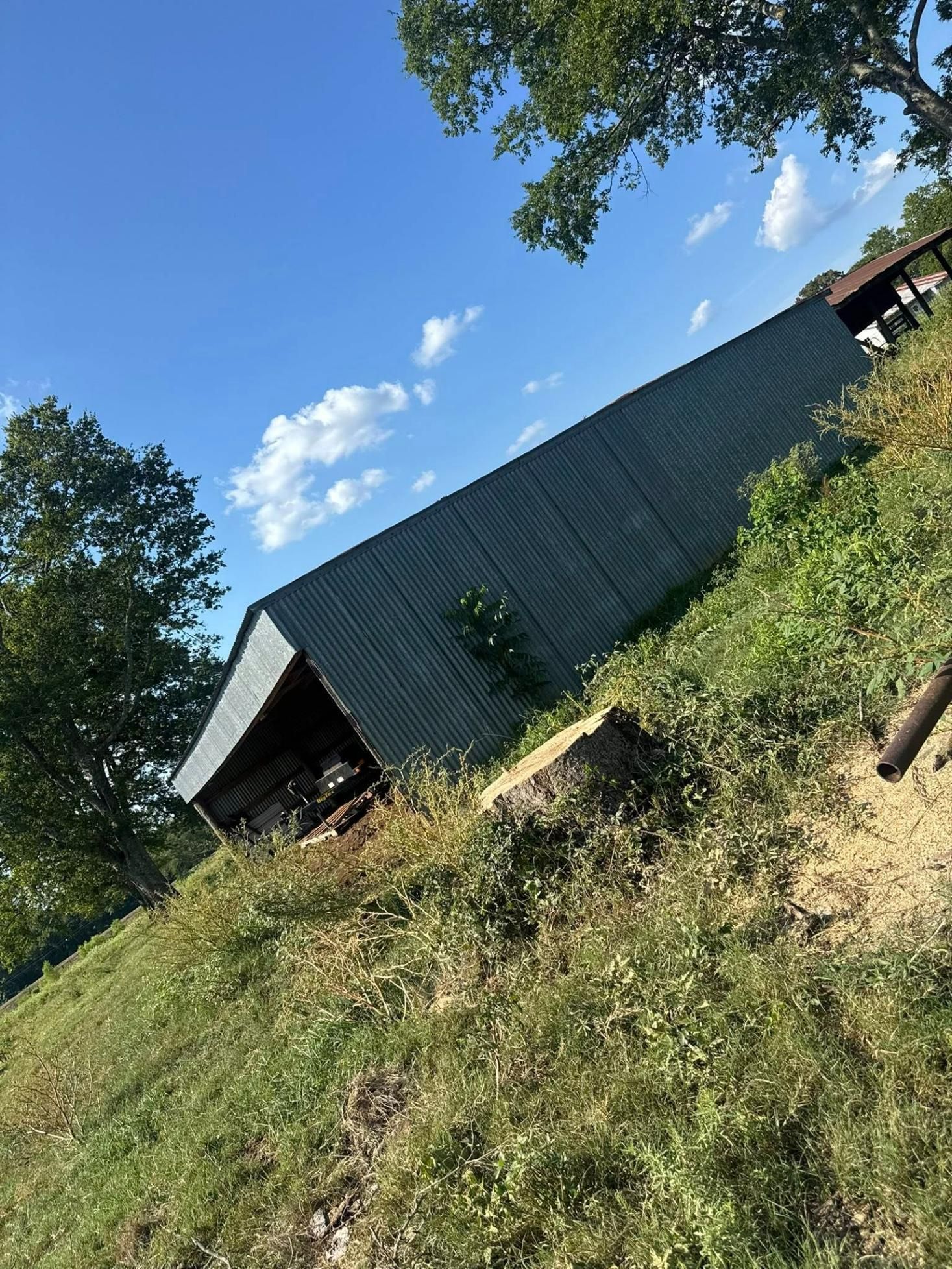 Green metal-roofed structure on a grassy hillside under a blue sky.