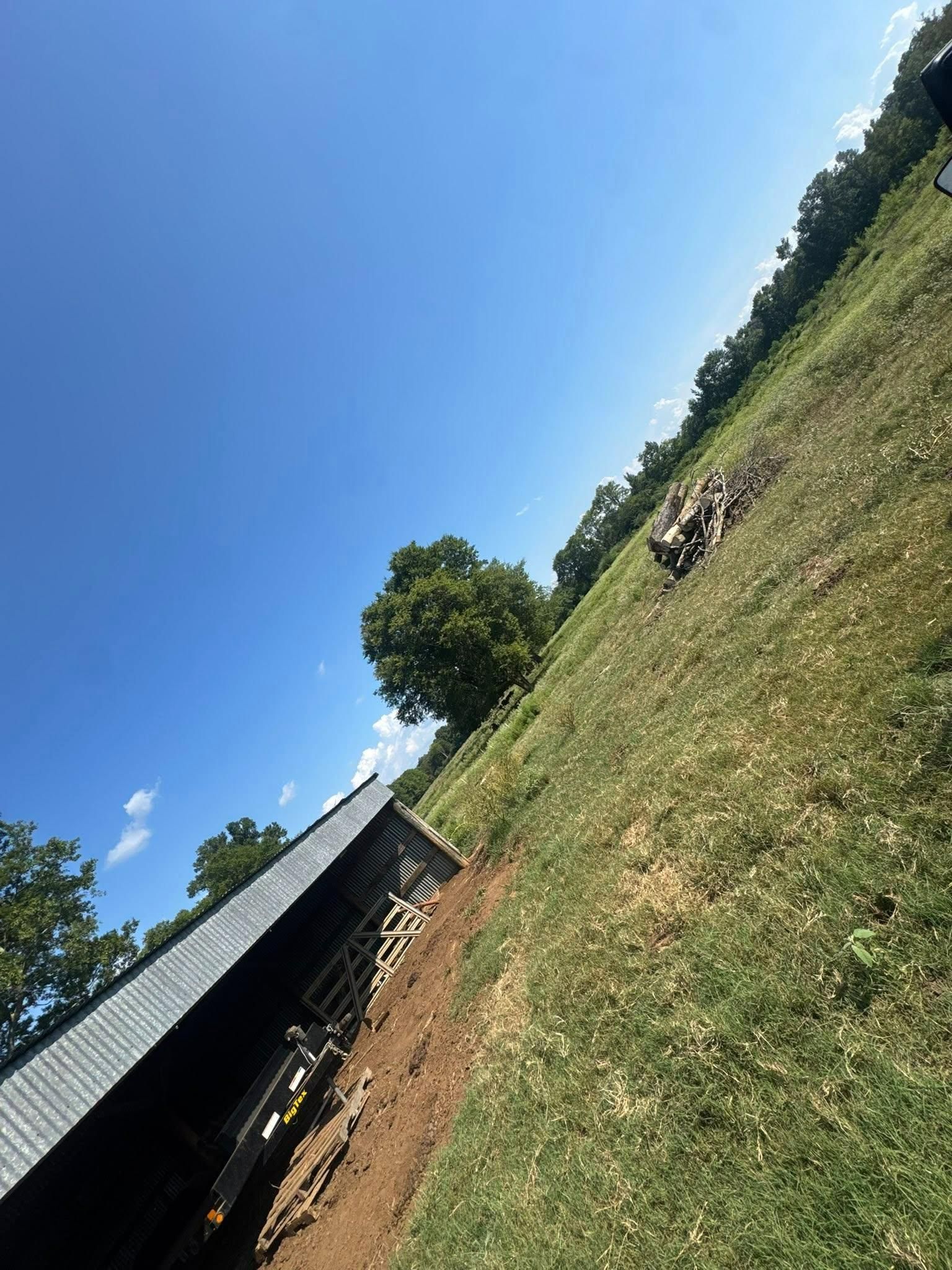 Grassy field and building with blue sky. Dirt path alongside the building, trees in background.