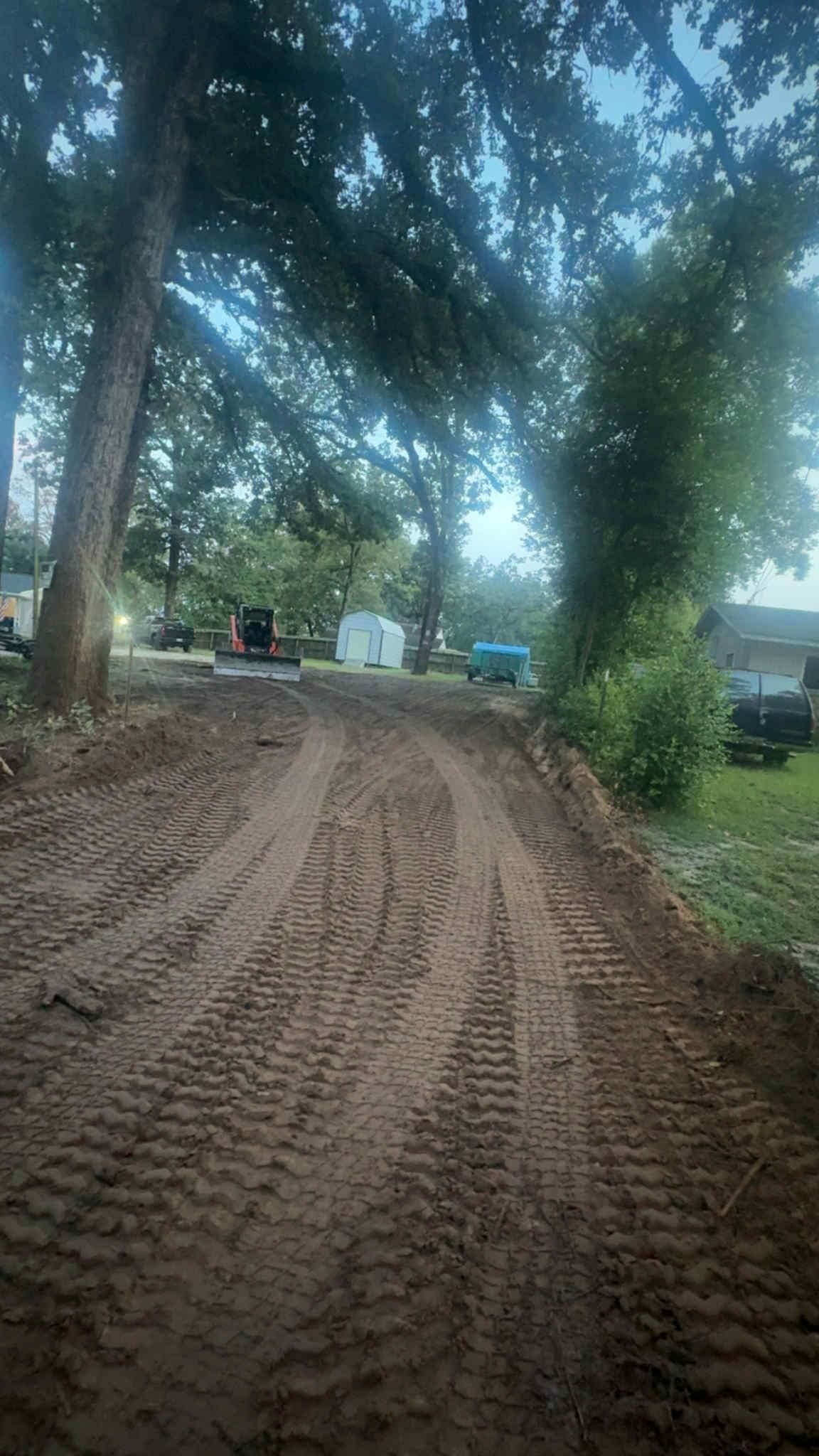 Dirt path with tire tracks leading towards trees and a small building.