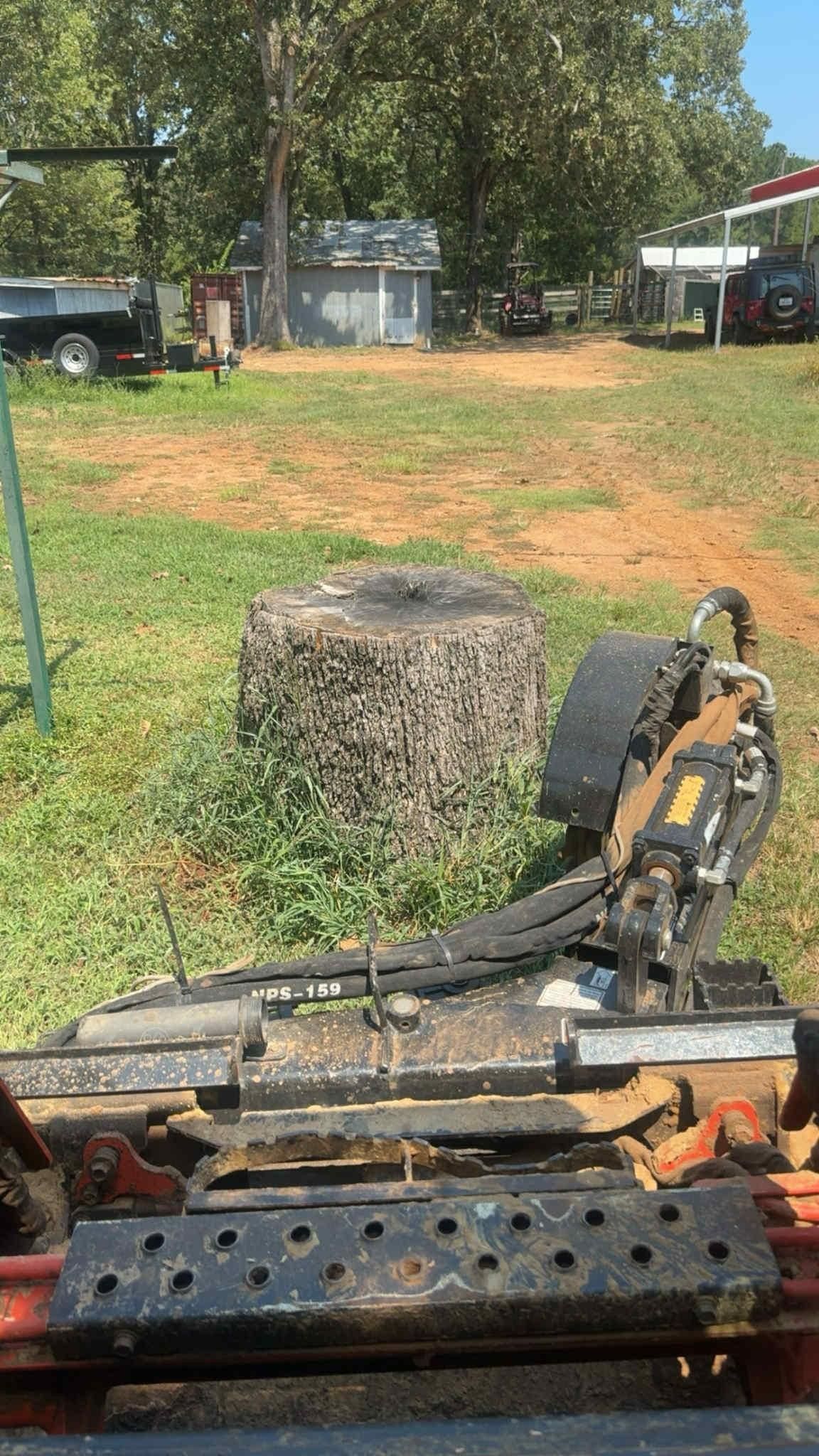 A stump grinding machine in a grassy yard, facing a large tree stump.