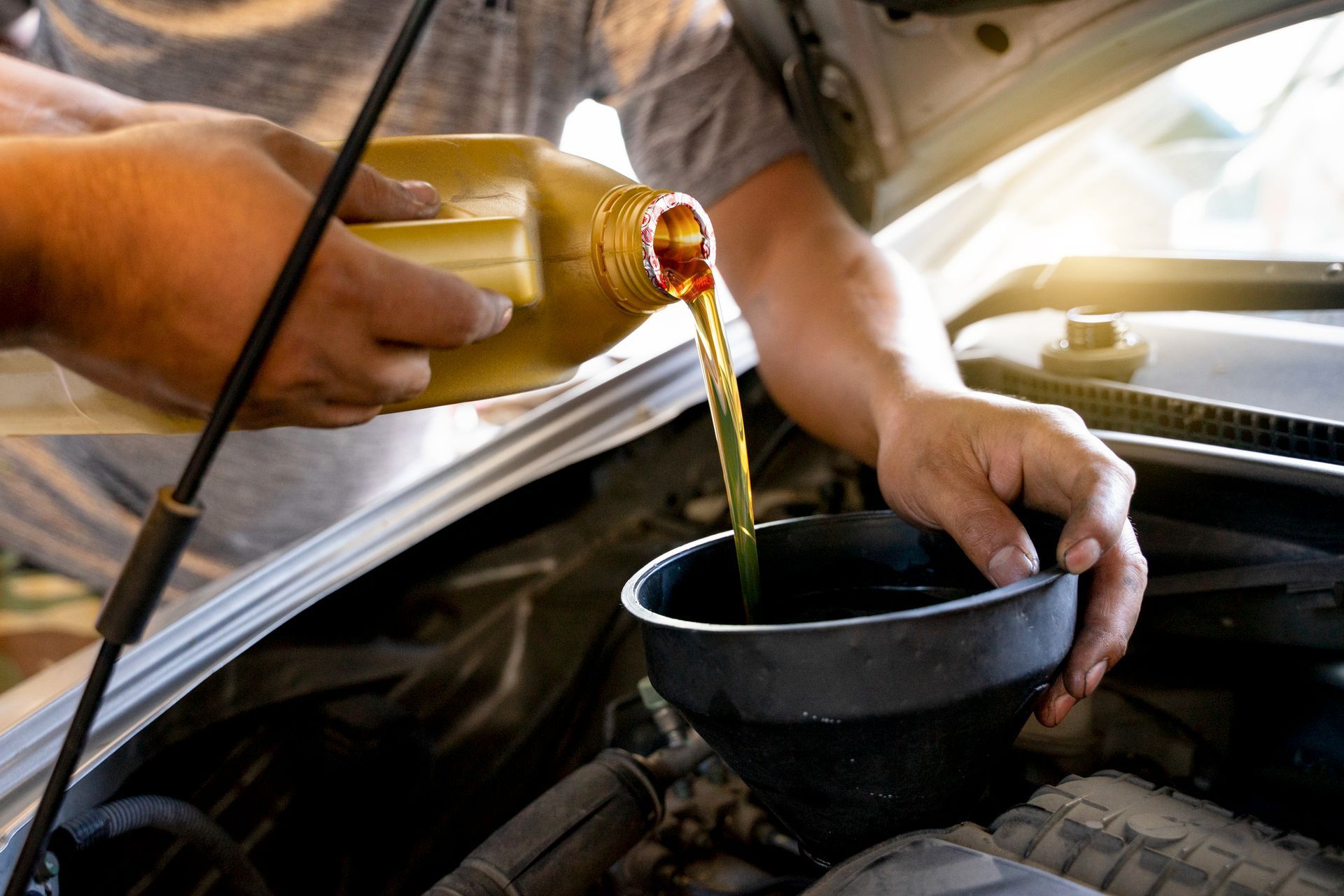 A man is pouring oil into a bowl under the hood of a car.