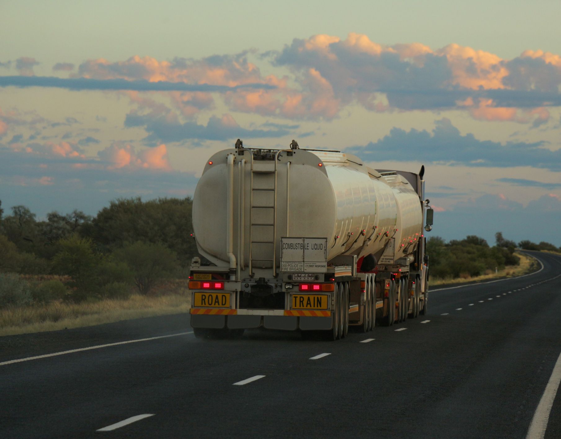 A tanker truck is driving down a highway at sunset.