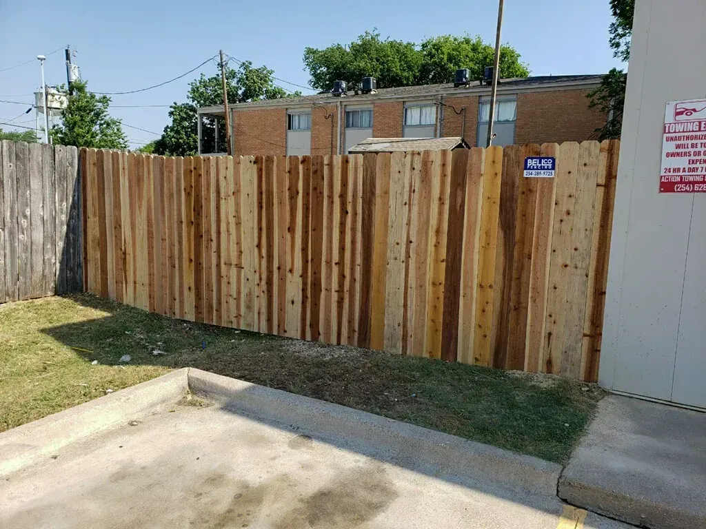 Wooden fence in front of apartment buildings on a sunny day.