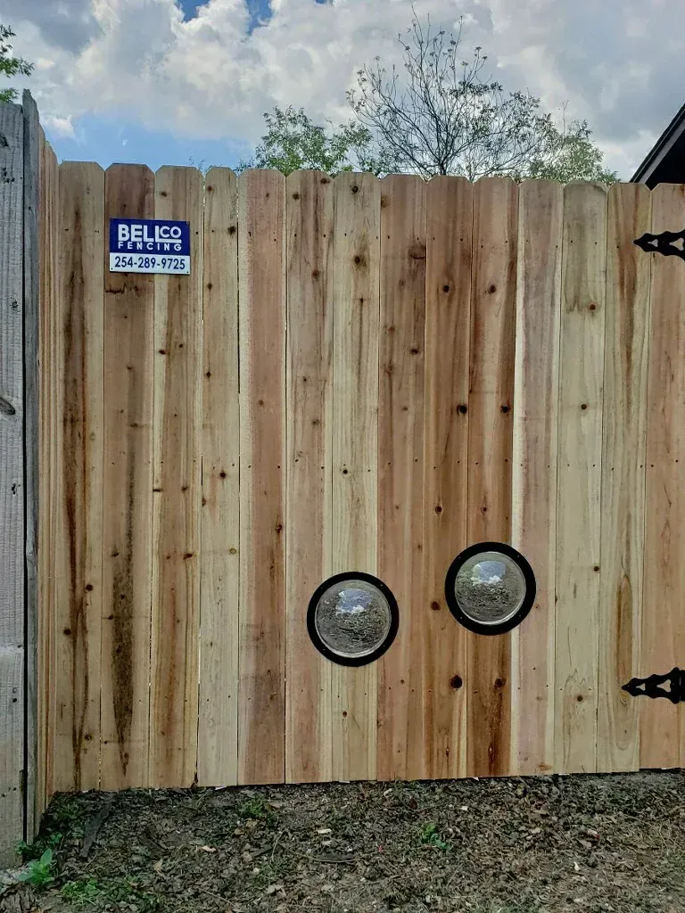 Wooden backyard gate with two circular windows for pets.
