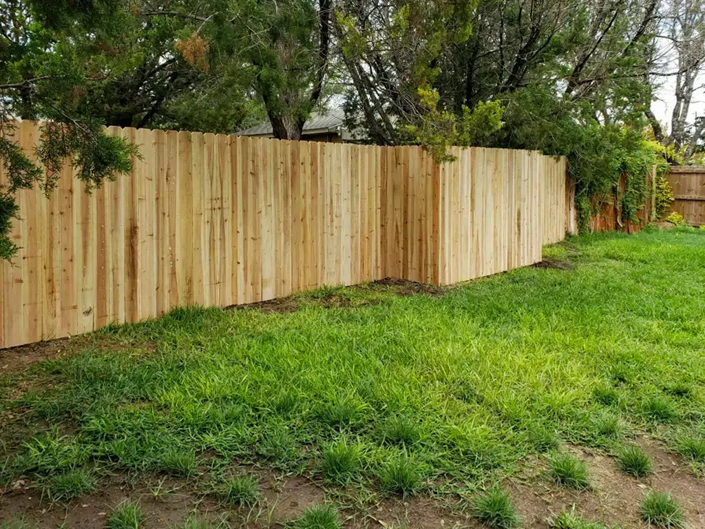 Wooden fence in a backyard with green grass and trees in the background.