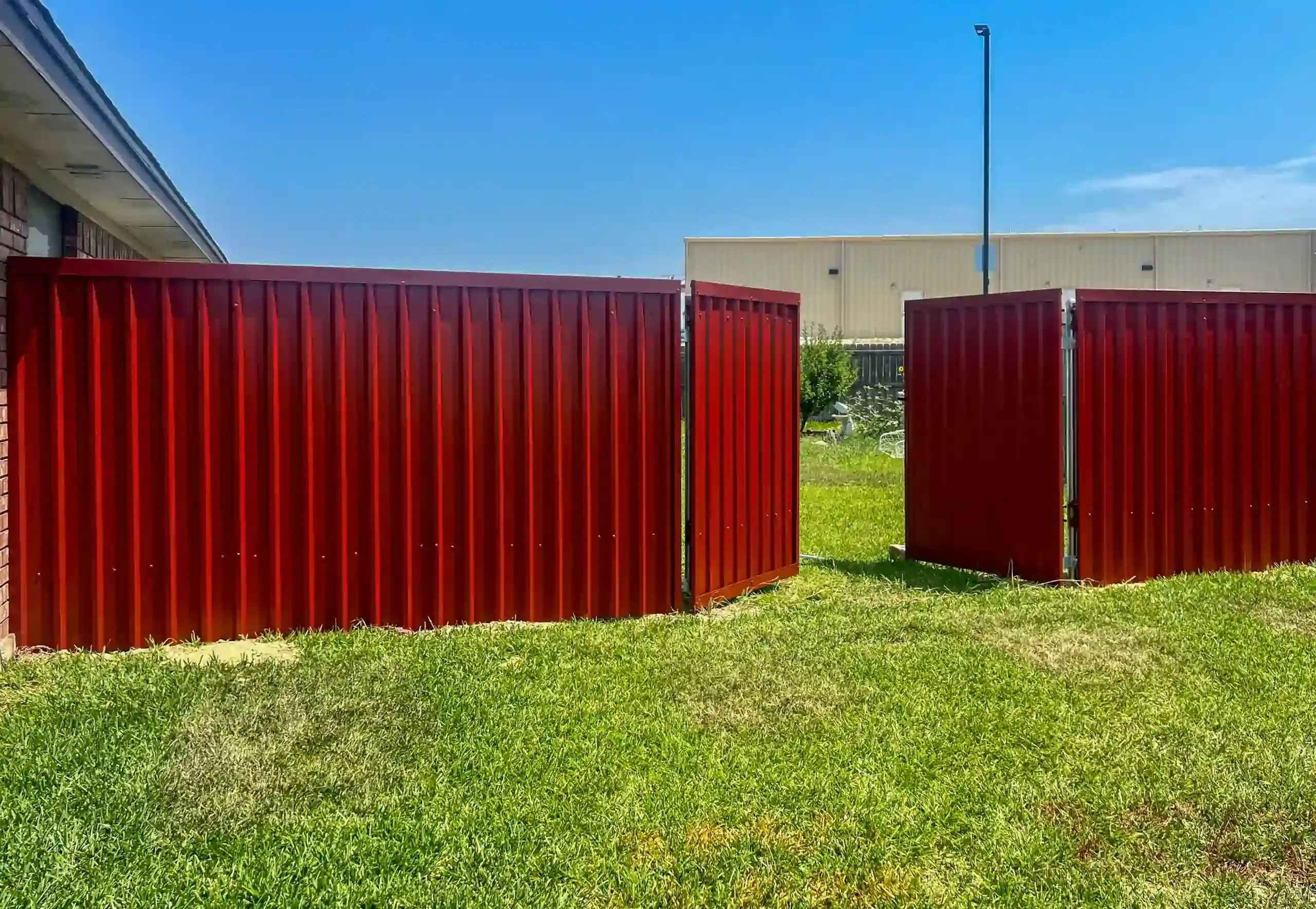Red corrugated metal fencing in a grassy area against a blue sky.