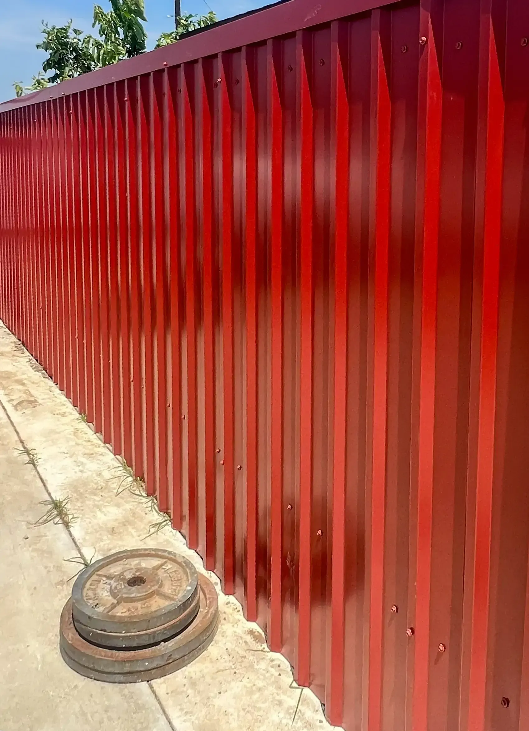Red corrugated metal fence with two rusty weight plates.
