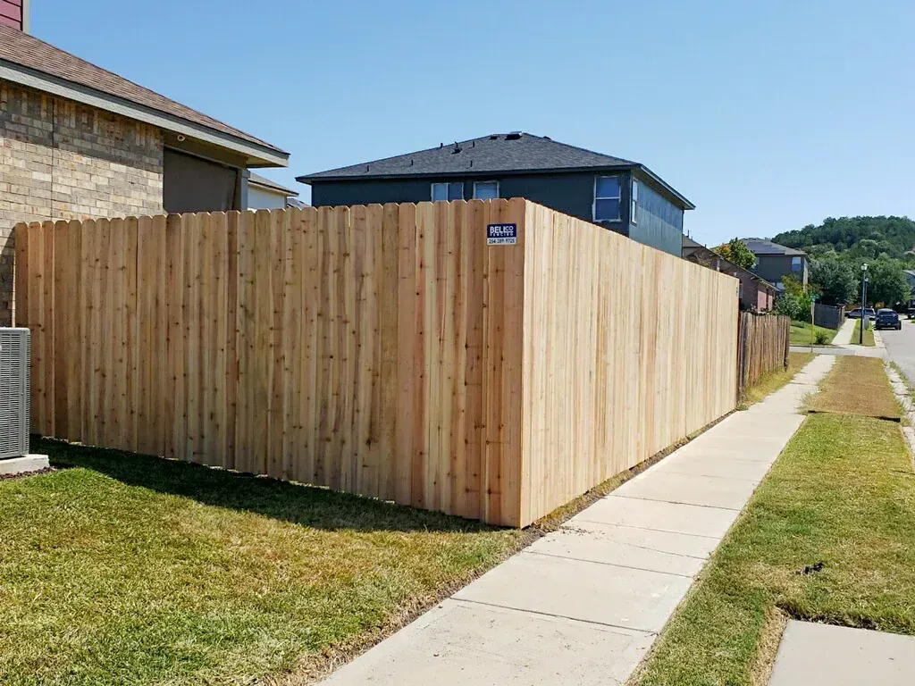 Wooden fence along a sidewalk, separating a yard from the street, sunny day.