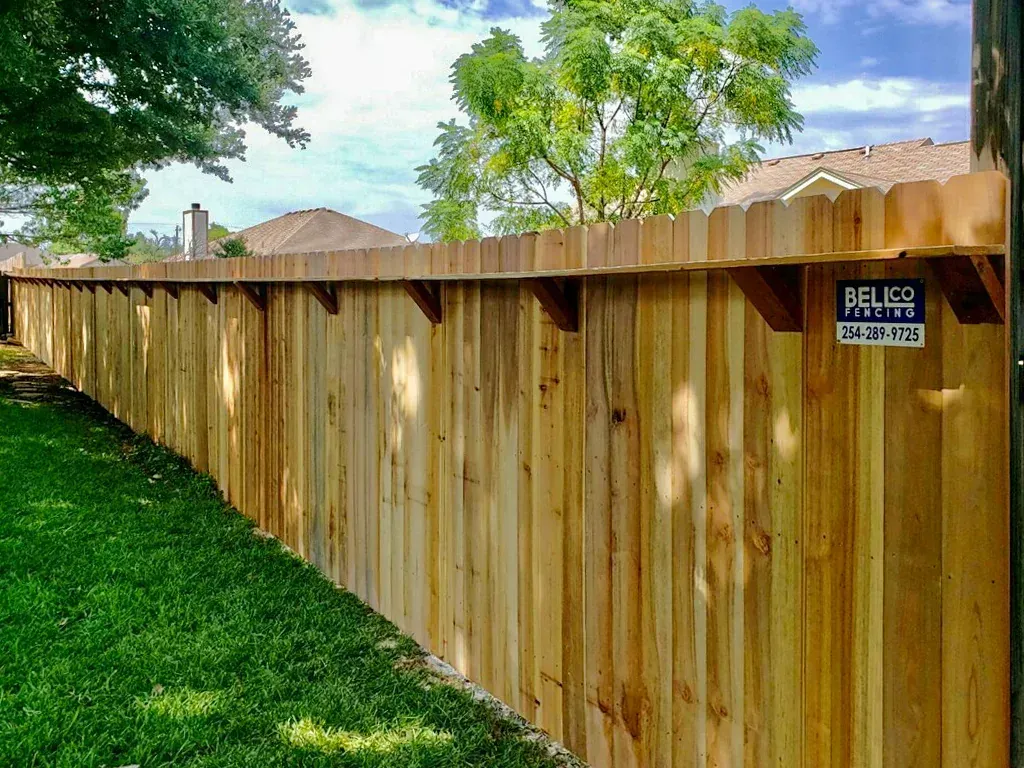 Wooden privacy fence along a green lawn, under a bright blue sky.