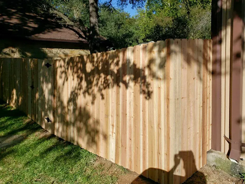 Wooden fence with shadow of tree on it in a grassy yard.