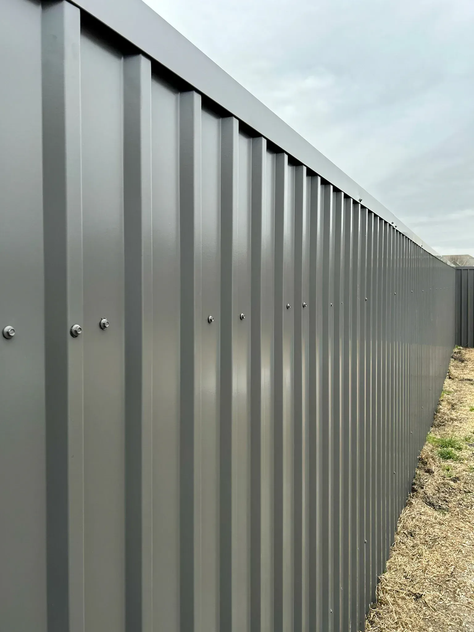 Gray metal fence with vertical ridges, against a cloudy sky.