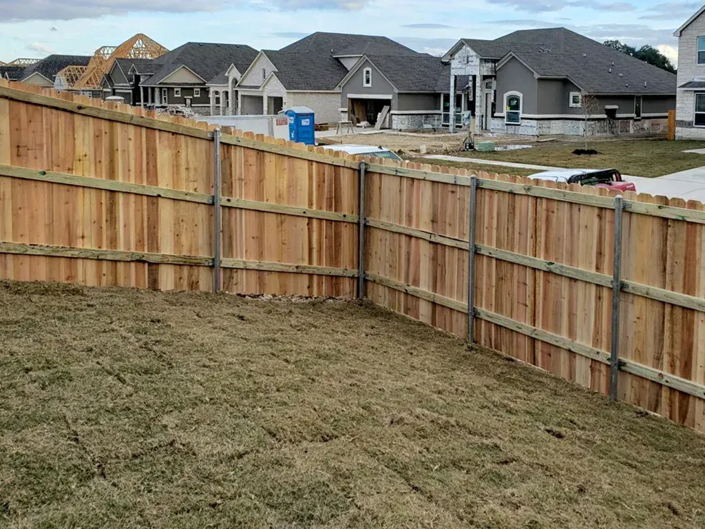 Wooden fence enclosing a grassy yard; new houses under construction in the background.