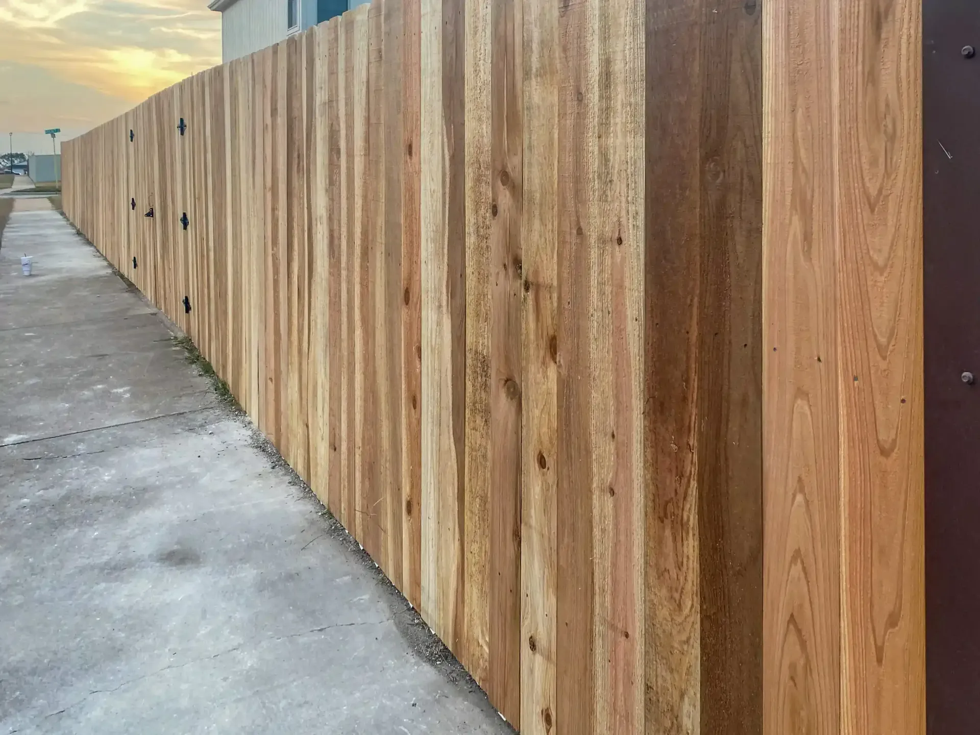 Wooden fence along a concrete walkway, exterior view, with a sunset in the background.