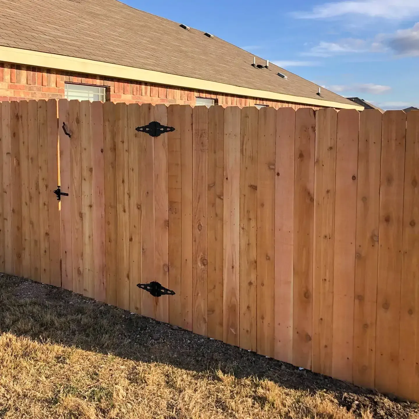 Wooden fence with black hardware in front of a brick house.