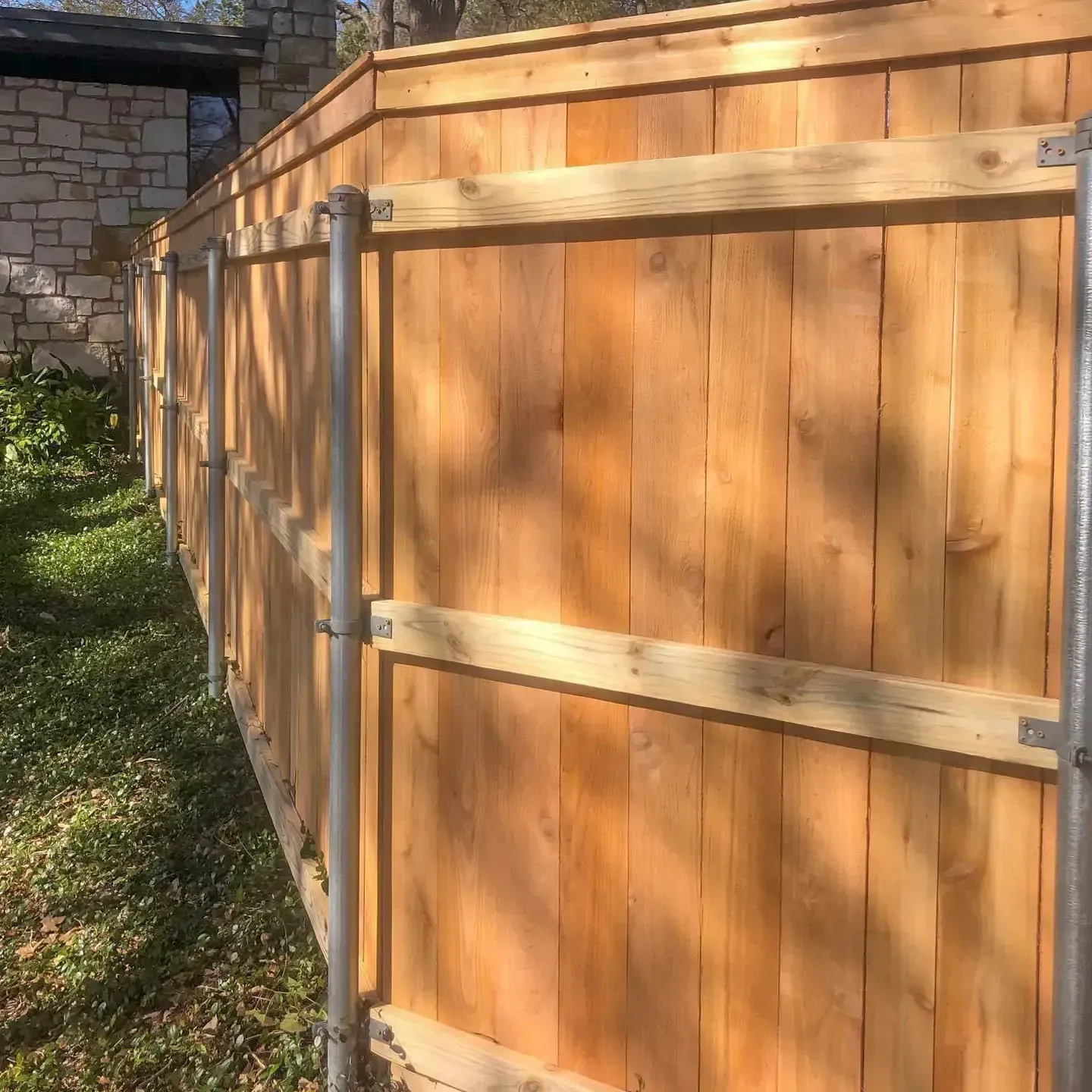 Wooden fence with metal posts, panels, and horizontal wooden supports along a grassy area.