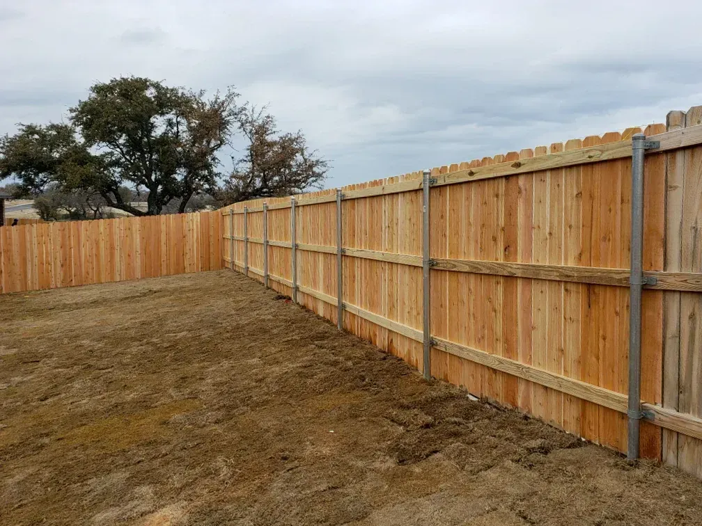 Wooden fence enclosing a brown yard under a cloudy sky.