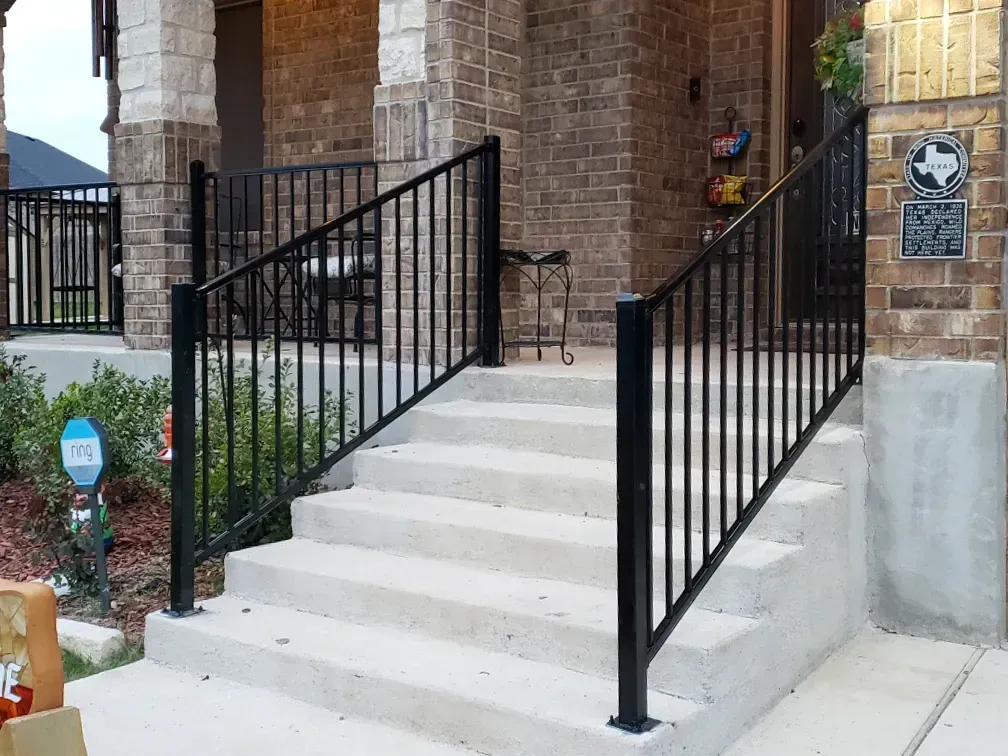 Black metal railing on concrete steps leading to a brick home's front porch.