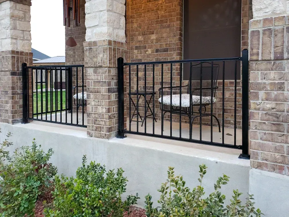Black metal railing on a porch with brick and stone pillars, and shrubs in front.