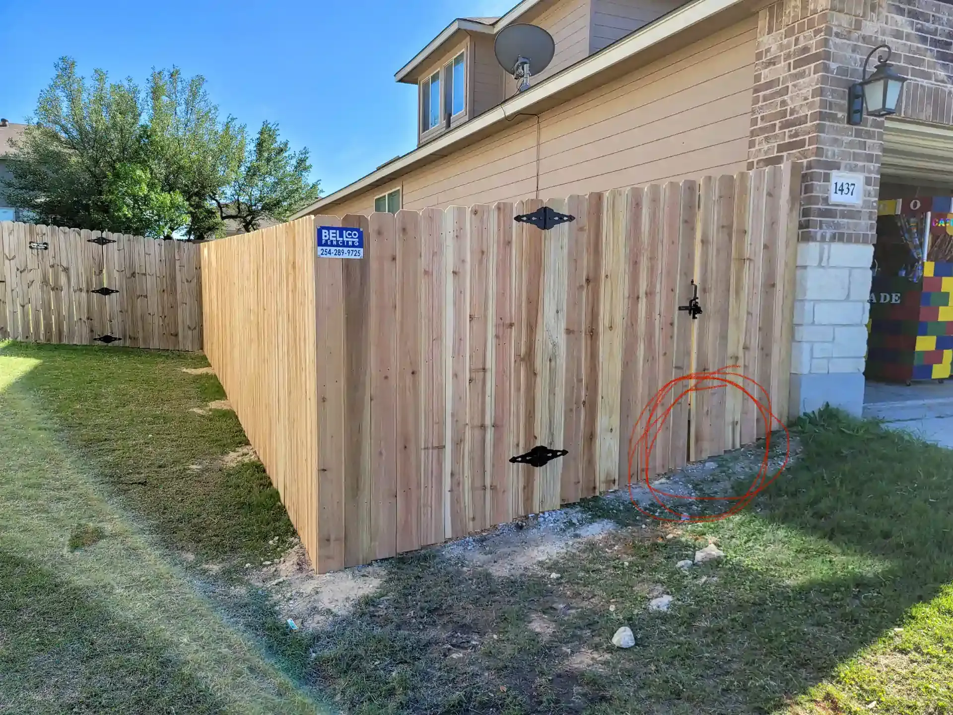 Wooden fence surrounding a grassy yard next to a beige house, orange conduit visible.