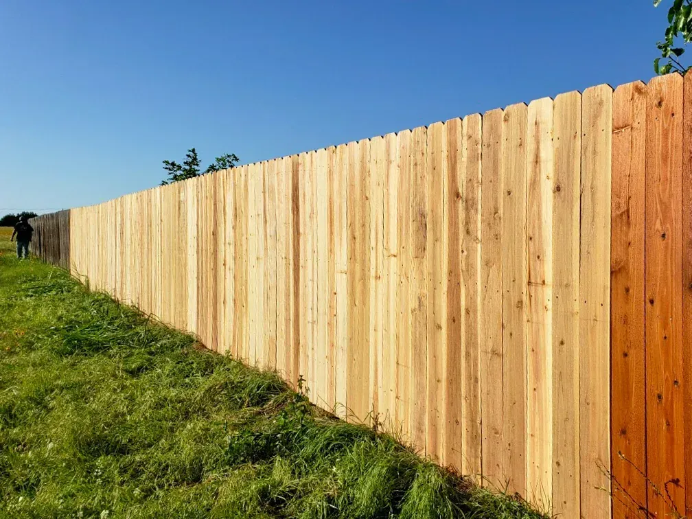 Wooden fence in a grassy field against a blue sky, with a person standing near the left.
