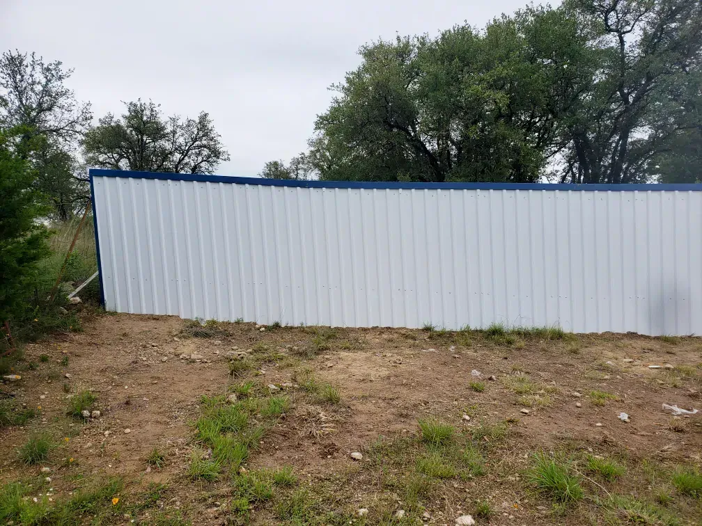 White metal building with blue trim, set in a yard with sparse grass and trees in the background.