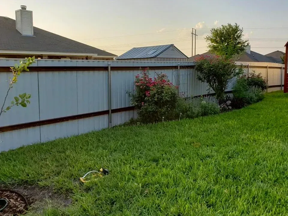 Backyard with a metal fence, green lawn, and flower bed.