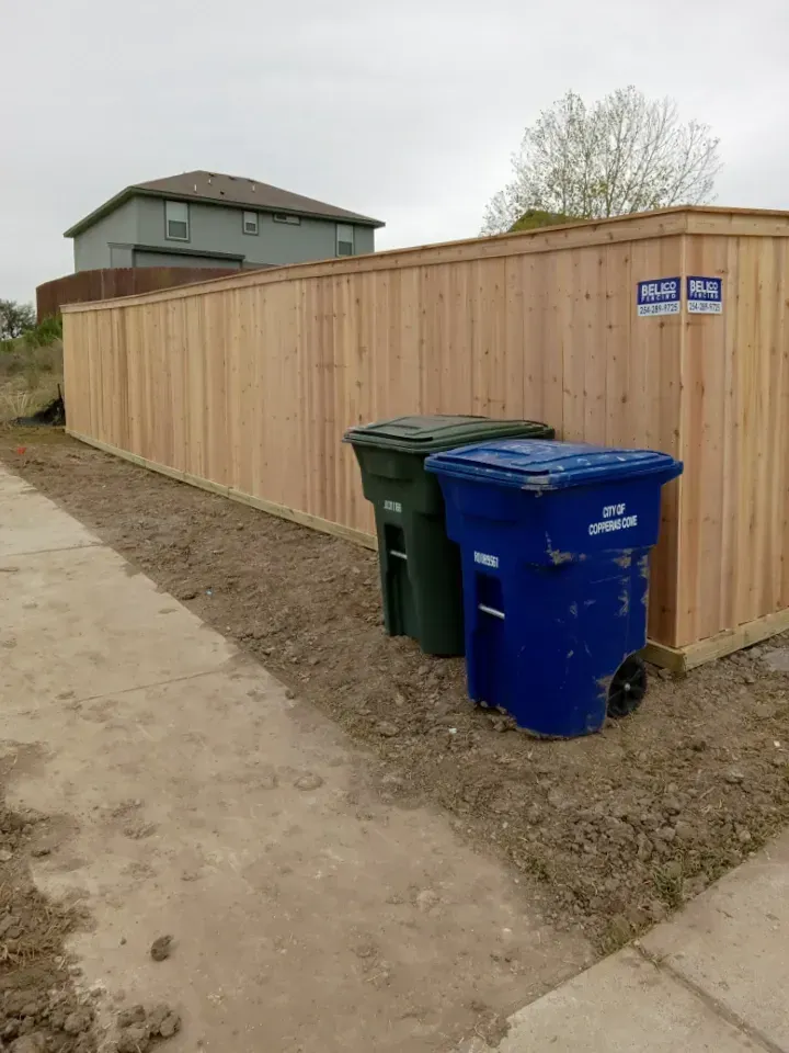 Wooden fence with two trash bins beside it.