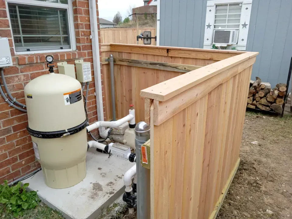 Pool equipment enclosed by a wooden fence, next to a brick building.