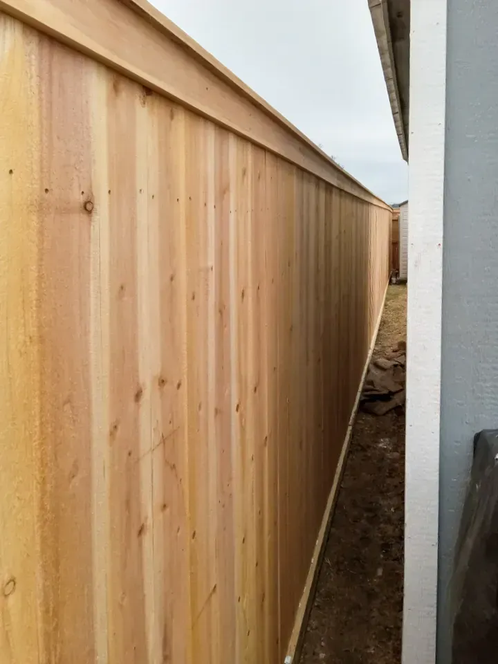Wooden fence alongside a building. Brown wood planks, overcast sky.