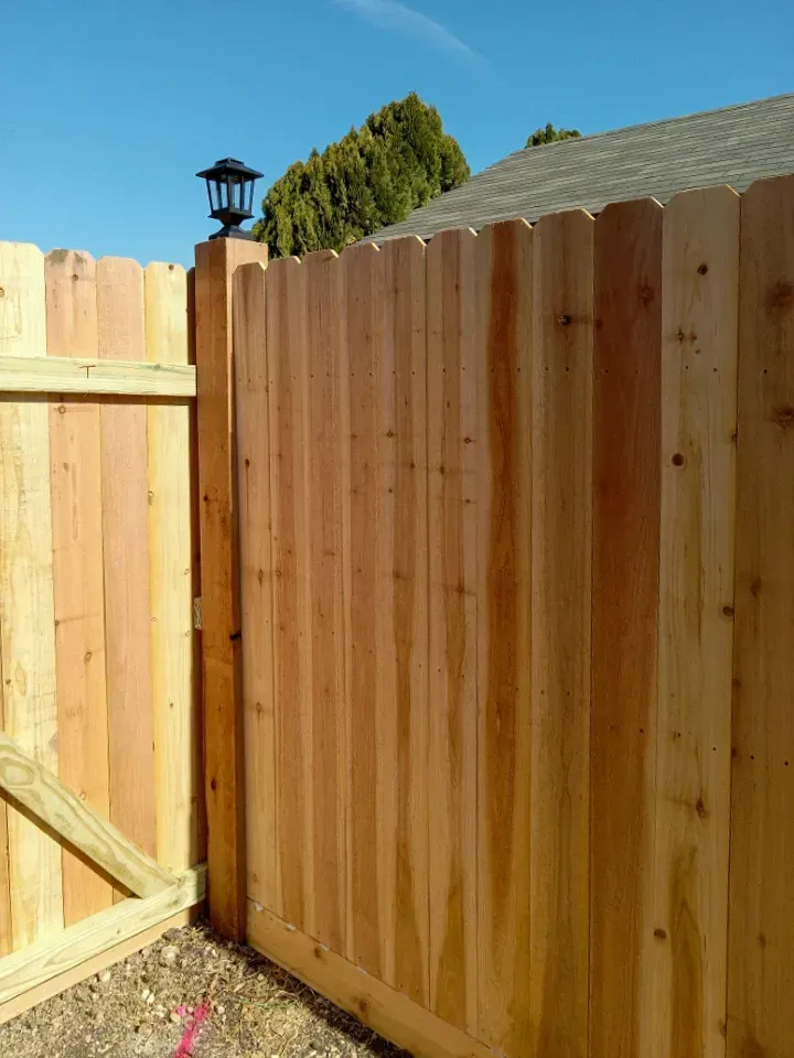 Wooden fence and gate with a decorative post-mounted light against a blue sky.