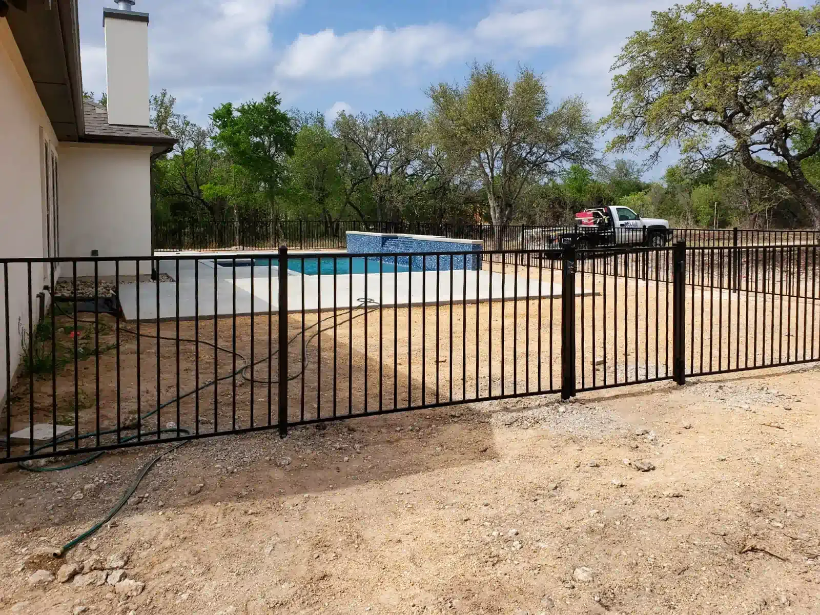 Black metal fence surrounding a pool and a house with a beige exterior, set outdoors.