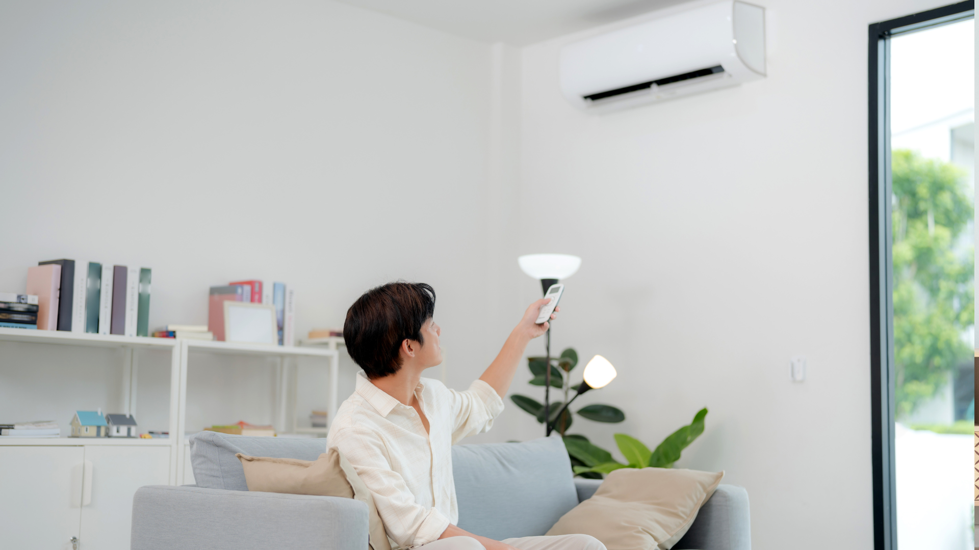 A man in a plaid shirt and green pants is installing a thermostat on a wall.