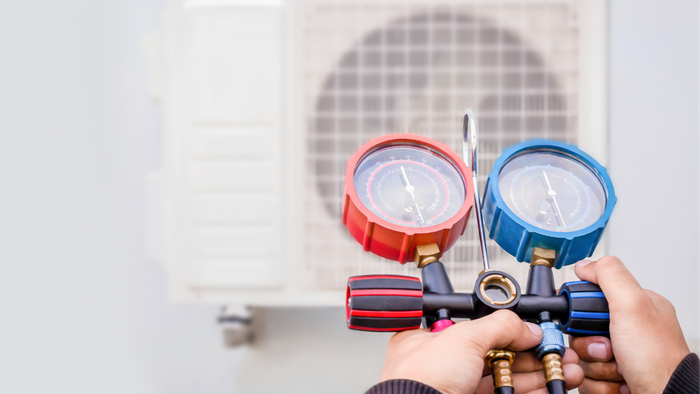 A person is holding a pair of gauges in front of an air conditioner.