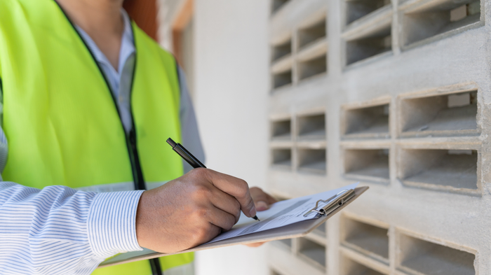 A man in a yellow vest is writing on a clipboard with a pen.