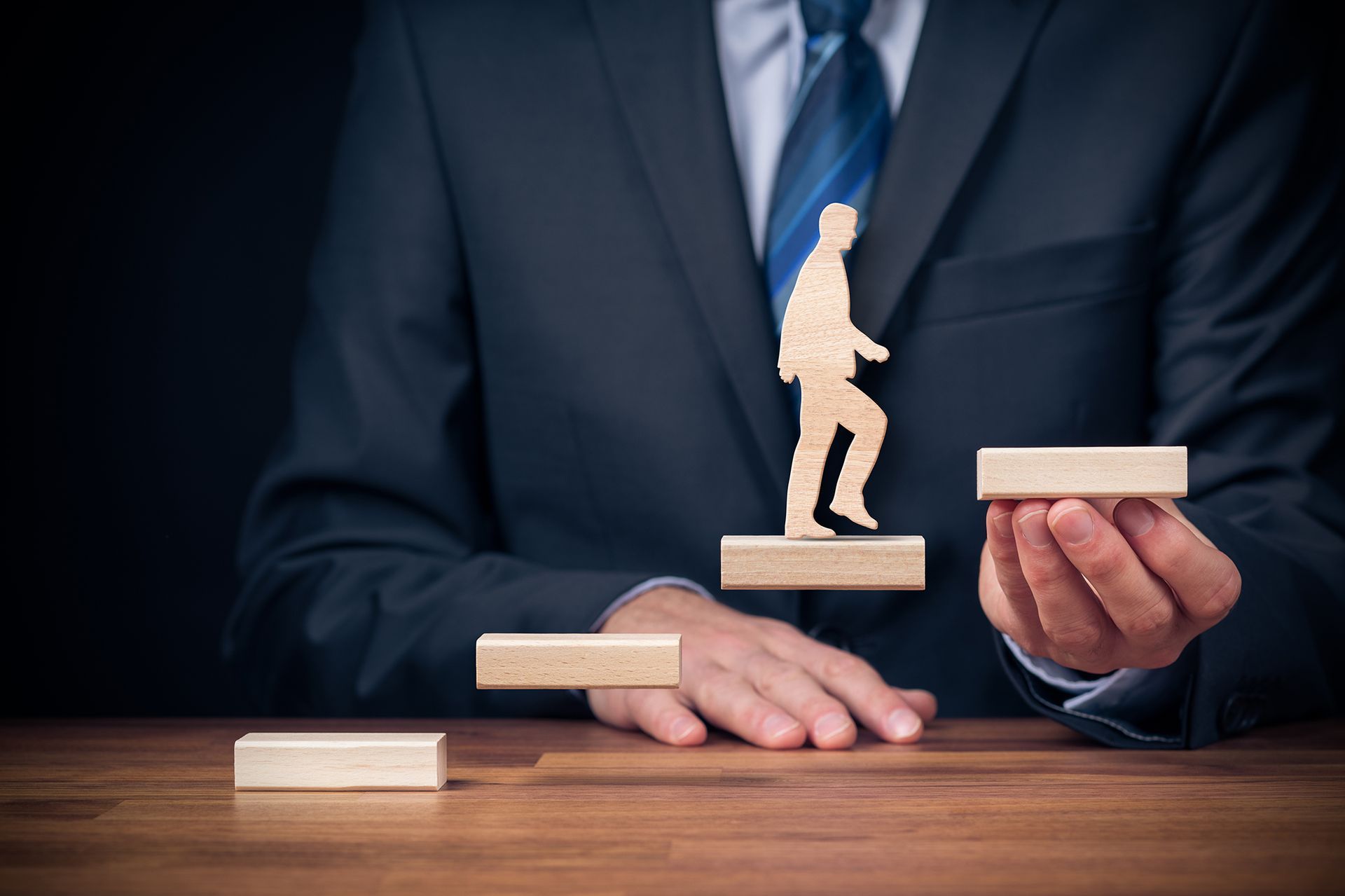 A man in a suit and tie is holding a wooden staircase with a man walking up it.