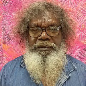 A man with glasses and a beard is standing in front of a pink background.