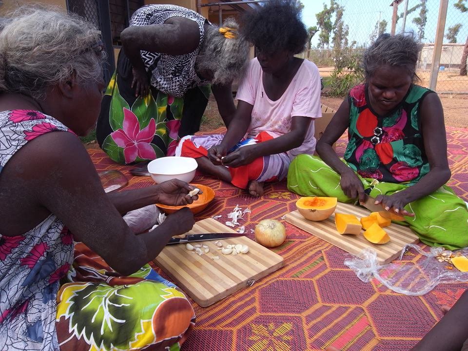 A group of women are sitting on the ground preparing food