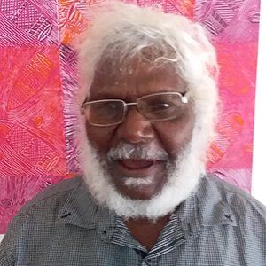 A man with a beard and glasses is smiling in front of a pink wall.