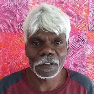 A man with white hair and a beard is standing in front of a colorful wall.