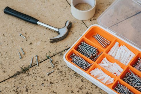 Hammer and assorted screws and nails in orange organizer trays on a dusty work surface