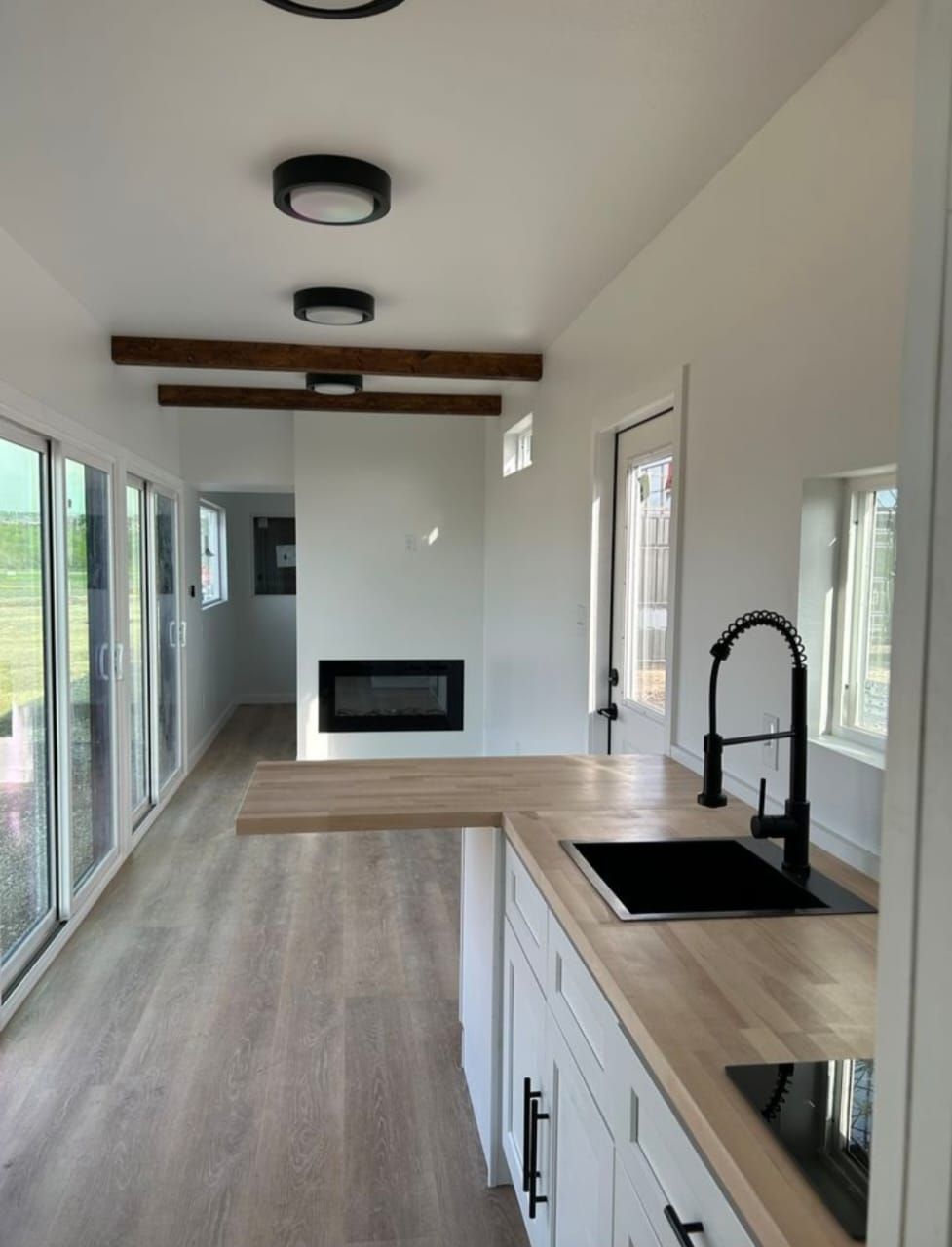 Cocina moderna con gabinetes blancos, encimeras de madera, grifo negro, chimenea y puertas corredizas de vidrio.