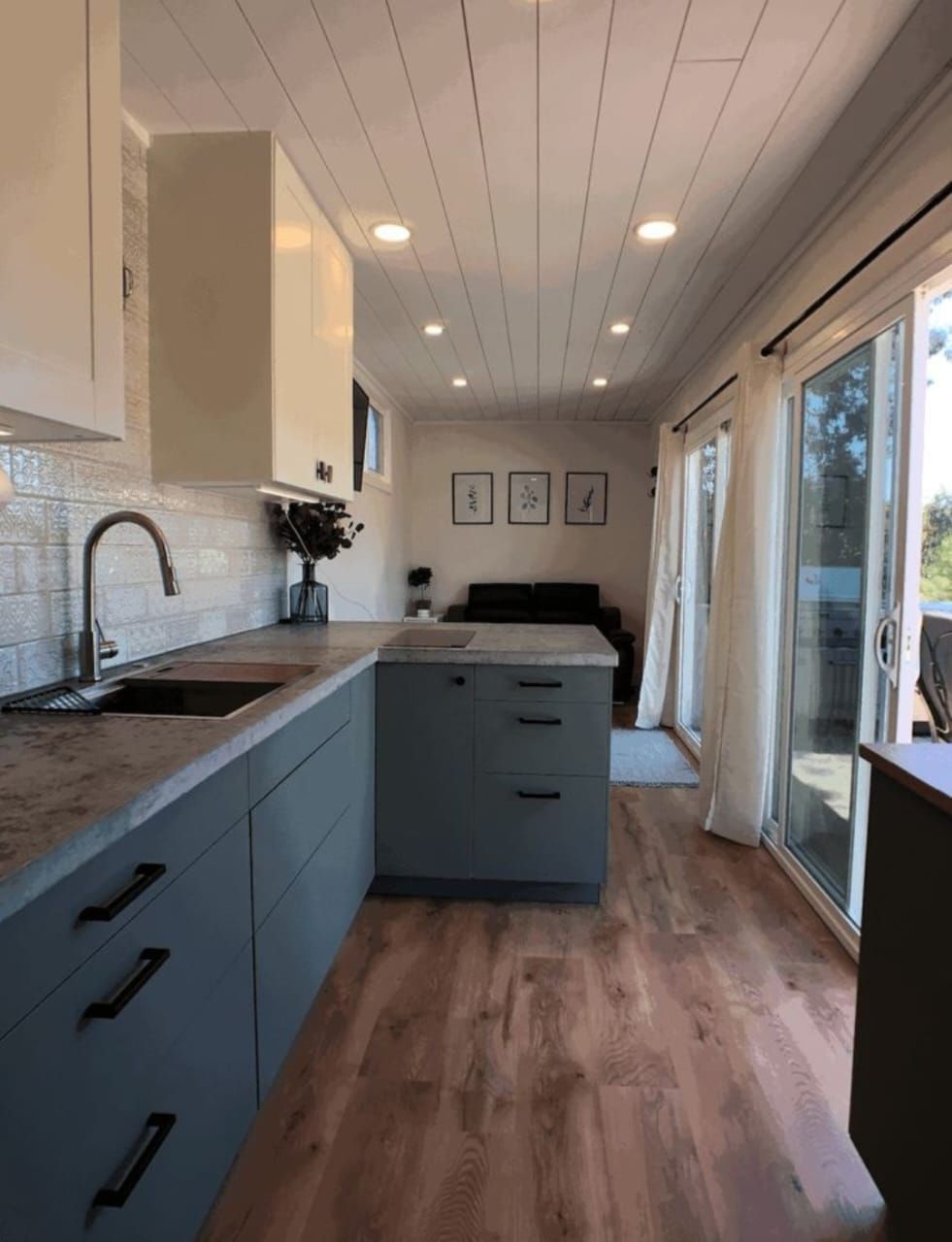 Cocina con gabinetes azules, encimeras grises, techo blanco y puertas corredizas de vidrio que dan a una terraza.