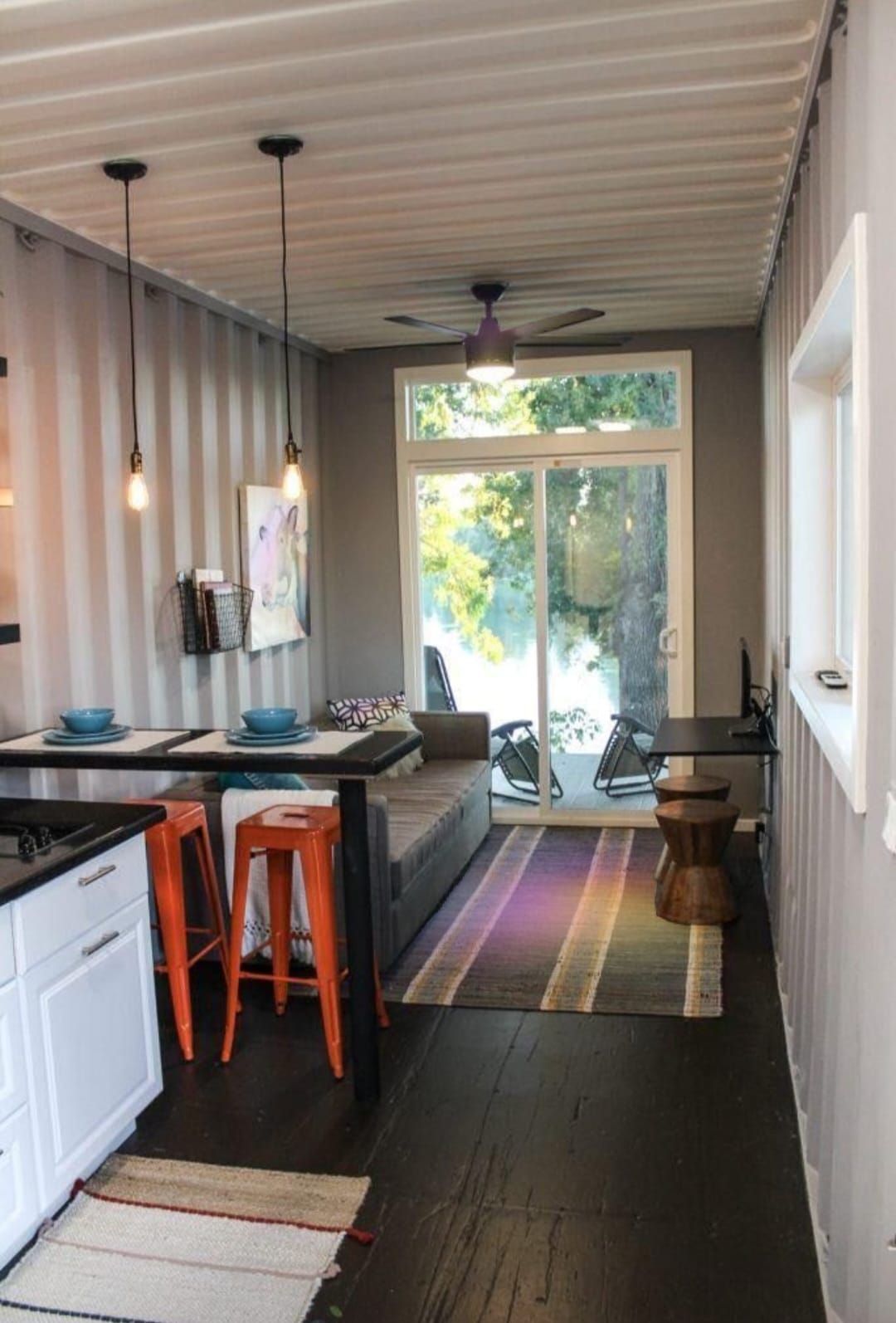 Interior de un contenedor marítimo reutilizado. Sala de estar con cocina, comedor y acceso al exterior.