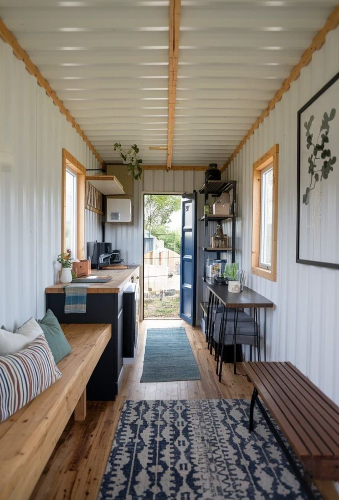 Interior de una casa contenedor con cocina, comedor y zona de estar. Madera clara y paredes blancas.