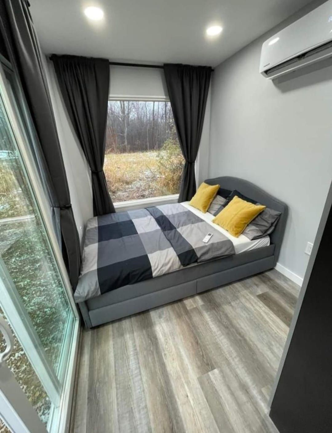 Dormitorio con paredes grises, cama y edredón estampado; ventana con cortinas oscuras; aire acondicionado en la pared.