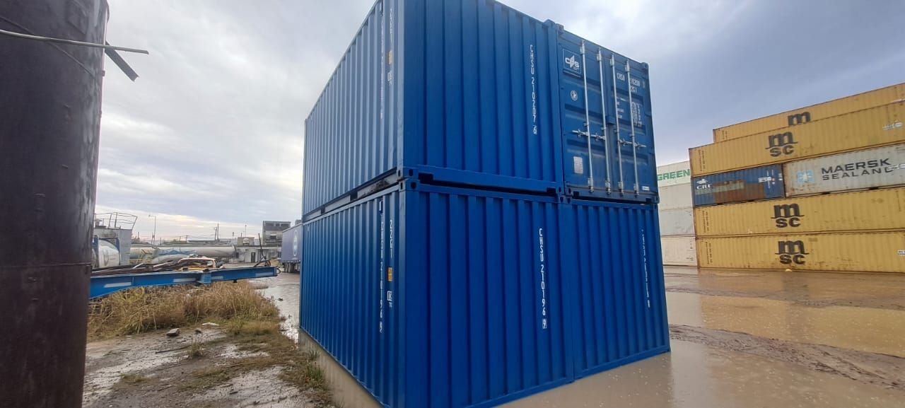 Dos contenedores de envío azules apilados al aire libre cerca de otros contenedores amarillos.