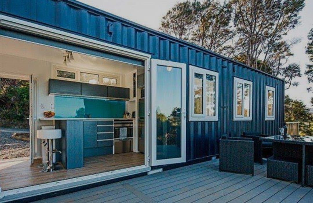 Casa contenedor de envío azul con puerta abierta a la cocina y la terraza.