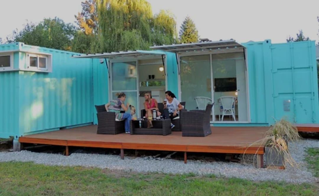 Tres personas están sentadas en muebles de exterior sobre una terraza de madera